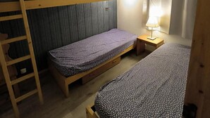 A small, compact room with bunk beds, a bedside table with a lamp, and a window with curtains.