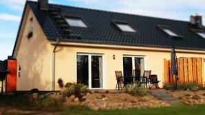 A modern house with a sloped roof, large windows, and a patio area with outdoor furniture. - Naturferienhof Märkisch Luch - Trapphenne (Märkisch Luch)