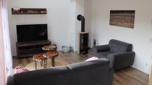 A modern living room with a flat-screen TV, grey sofas, wooden side tables, and a fireplace. - Naturferienhof Märkisch Luch - Trapphenne (Märkisch Luch)