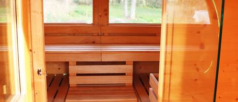 A wooden sauna with benches and a glass door, leading to an outdoor area.