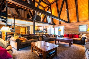 A spacious living area with a high ceiling, wooden beams, and a cozy fireplace. - Roosevelt Suite, The Roosevelt Suite at the Lodge (Story)