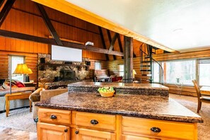A log cabin interior with a stone fireplace, wooden furniture, and a large kitchen island. - Roosevelt Suite, The Roosevelt Suite at the Lodge (Story)