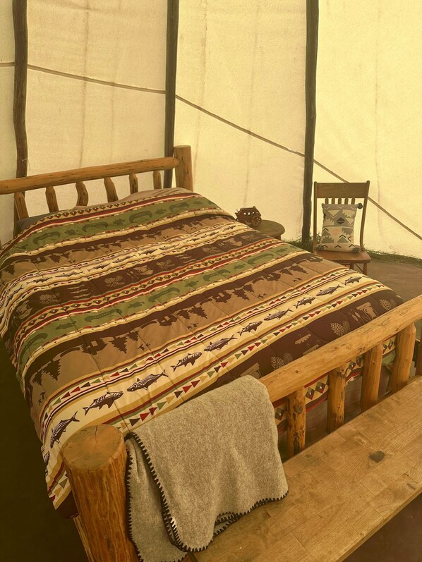 Una cama con una colcha estampada, un banco de madera y una mesita con un cojín.