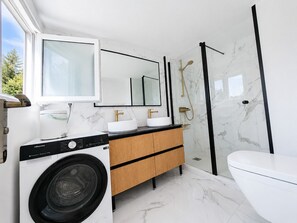 A modern bathroom with a washing machine, dual sinks, a toilet, and a glass shower enclosure.