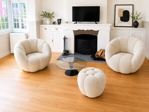 A living room with two armchairs, a glass coffee table, a fireplace, a TV, and a framed artwork.