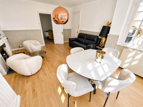 A modern living room with a round table, white armchairs, a black sofa, and a copper pendant light.