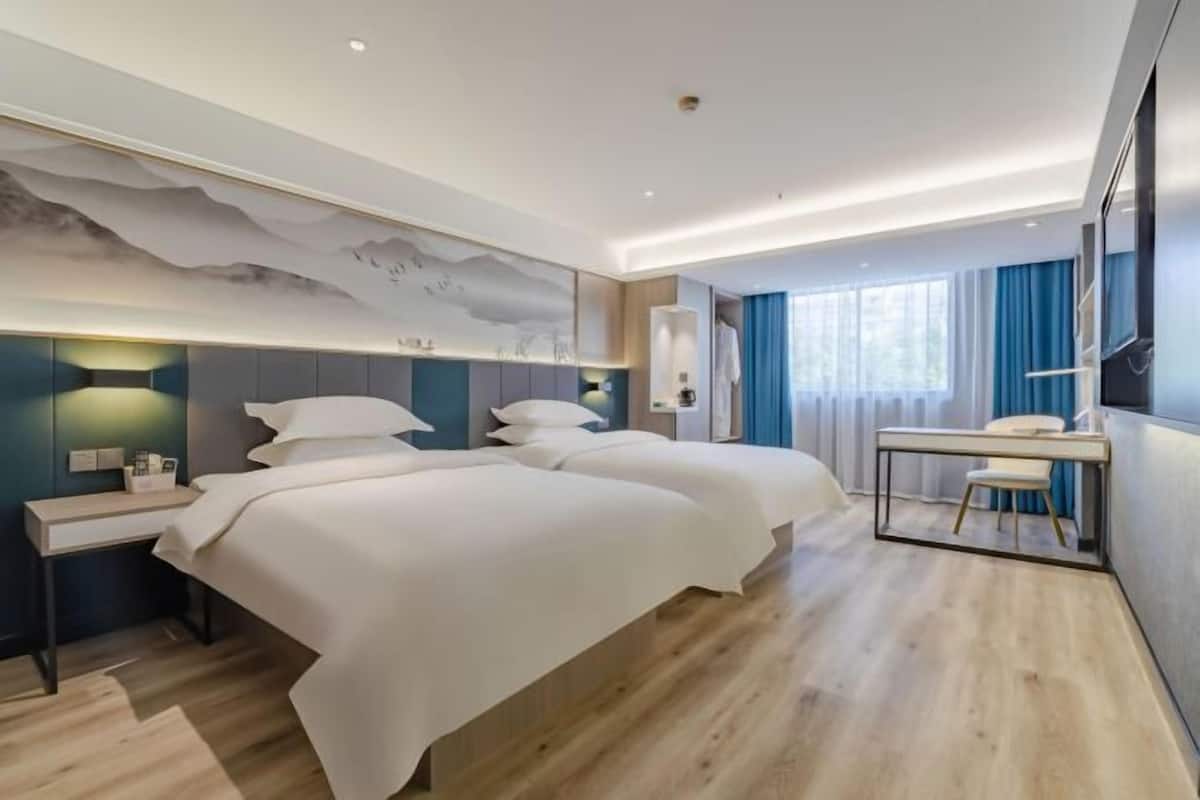 Une chambre d’hôtel moderne, dotée d’un grand lit, de tables de chevet, d’un bureau et offrant une vue sur l’extérieur.