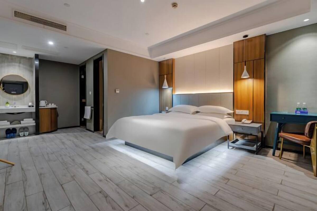 Une chambre d’hôtel moderne équipée d’un grand lit, d’un bureau, d’une chaise, d’une coiffeuse avec un miroir et d’un espace douche.
