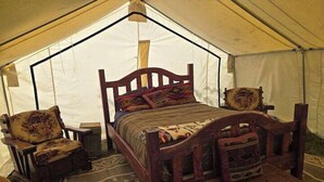 Une tente avec un lit en bois, deux chaises et une commode.