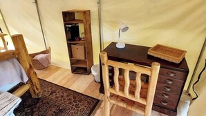A tented room with a wooden chair, a desk with drawers, a lamp, and a shelf with various items.