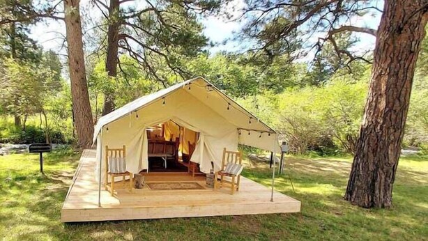 A tent with a wooden platform and chairs, surrounded by trees.