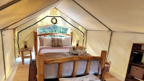 A tented accommodation with a bed, bedside tables, and a small seating area.
