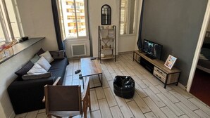 A living room with a sofa, a table, a TV, and a window with blinds. - Bright Apartment Near the Beach and Old Port (Marseille)