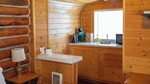 A cozy cabin-style kitchen with wooden walls, a window, a sink, and a stove.