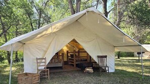 A tent with a simple layout, including a seating area with chairs and a table, and a storage box labeled 'FOOD'. - Homesteader Wall Tent, Homesteader Wall Tent by the Stream (Story)