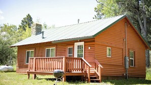 A wooden cabin with a porch, a chimney, and a metal grill in front. - Creekside Chalet, Private Creekside Chalet (Story)