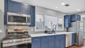 Una cocina moderna con armarios azules, electrodomésticos de acero inoxidable y un amplio ventanal con persianas.