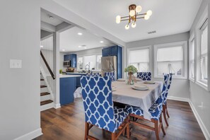 A modern kitchen with blue cabinets, a stainless steel refrigerator, and a dining area with a white table and blue patterned chairs.