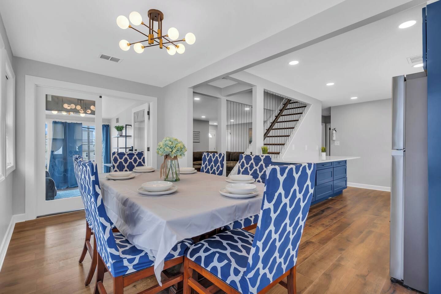 A modern dining area with a round table, blue patterned chairs, and a chandelier.