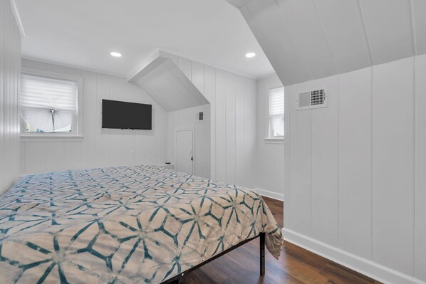 A bedroom with a bed, a TV mounted on the wall, and a window with blinds.