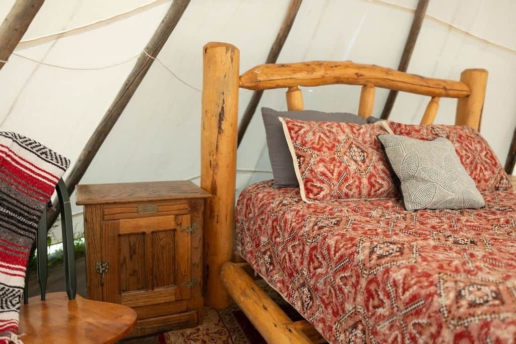 En mysig säng med mönstrat sänglinne, ett träfärgat sänggavel och ett litet träbord vid sängen med en låda.