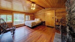 Une chambre aménagée dans un chalet en rondins, avec un lit, deux chaises, une table et un mur en pierre.