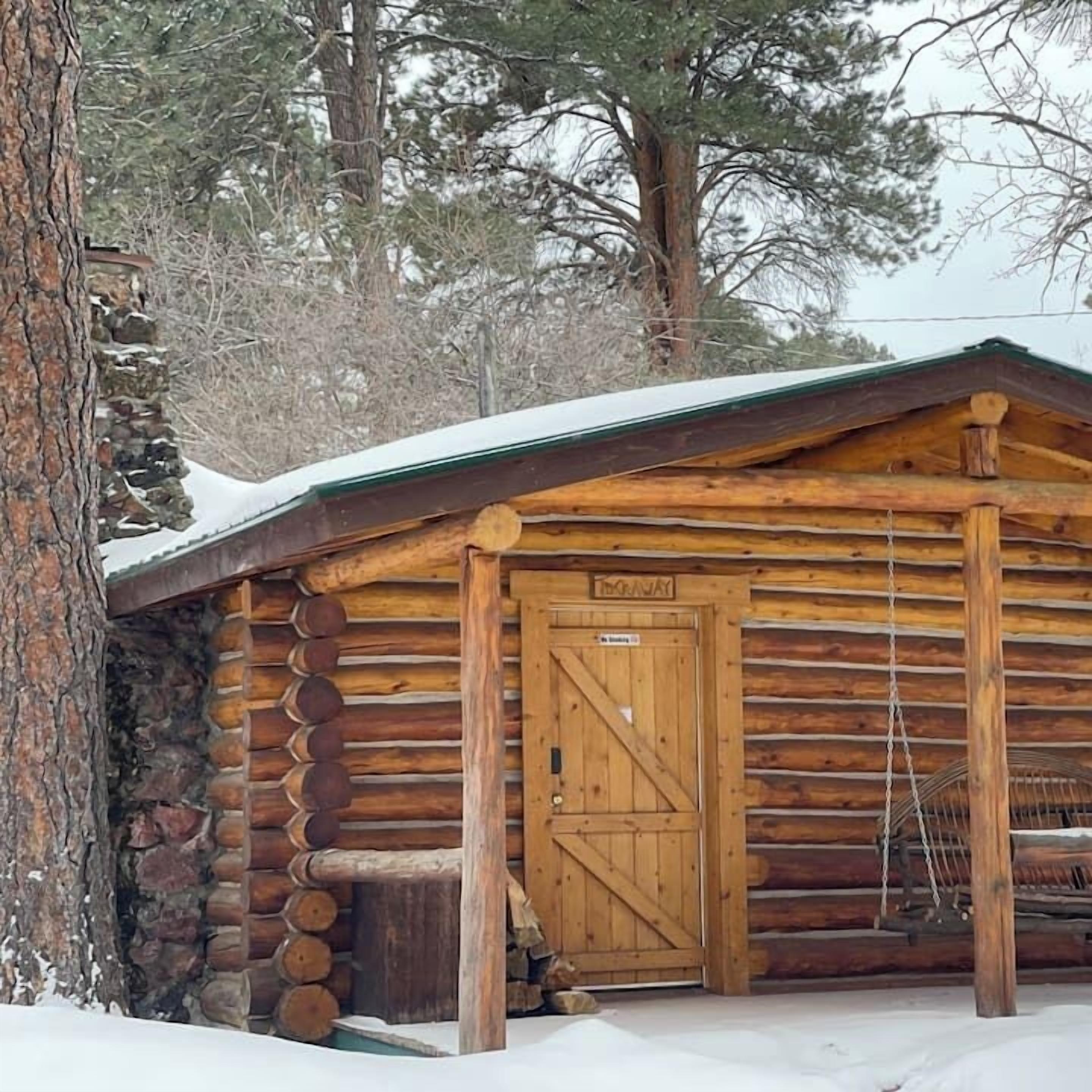 Una cabana de fusta amb una porta de fusta, una paret de pedra i un teulat cobert de neu.