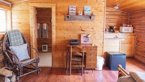 L’intérieur chaleureux d’un chalet, avec un revêtement mural en bois, un fauteuil à bascule, un bureau avec des tiroirs, une petite kitchenette et une étagère ornée d’objets décoratifs.