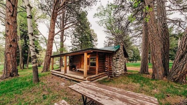 A rustic cabin with a stone foundation and wooden exterior, surrounded by tall trees. - Hideout Cabin, Rustic Hideout Cabin (Story)