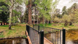 A wooden bridge over a calm stream, surrounded by trees and a grassy area. - Hideout Cabin, Rustic Hideout Cabin (Story)
