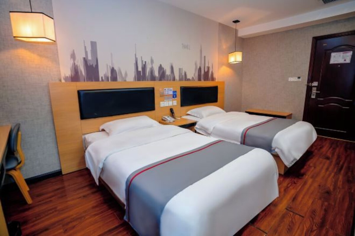 Quarto de hotel com duas camas, um mural da linha do horizonte da cidade, cabeceira de madeira, escrivaninha e uma cadeira.