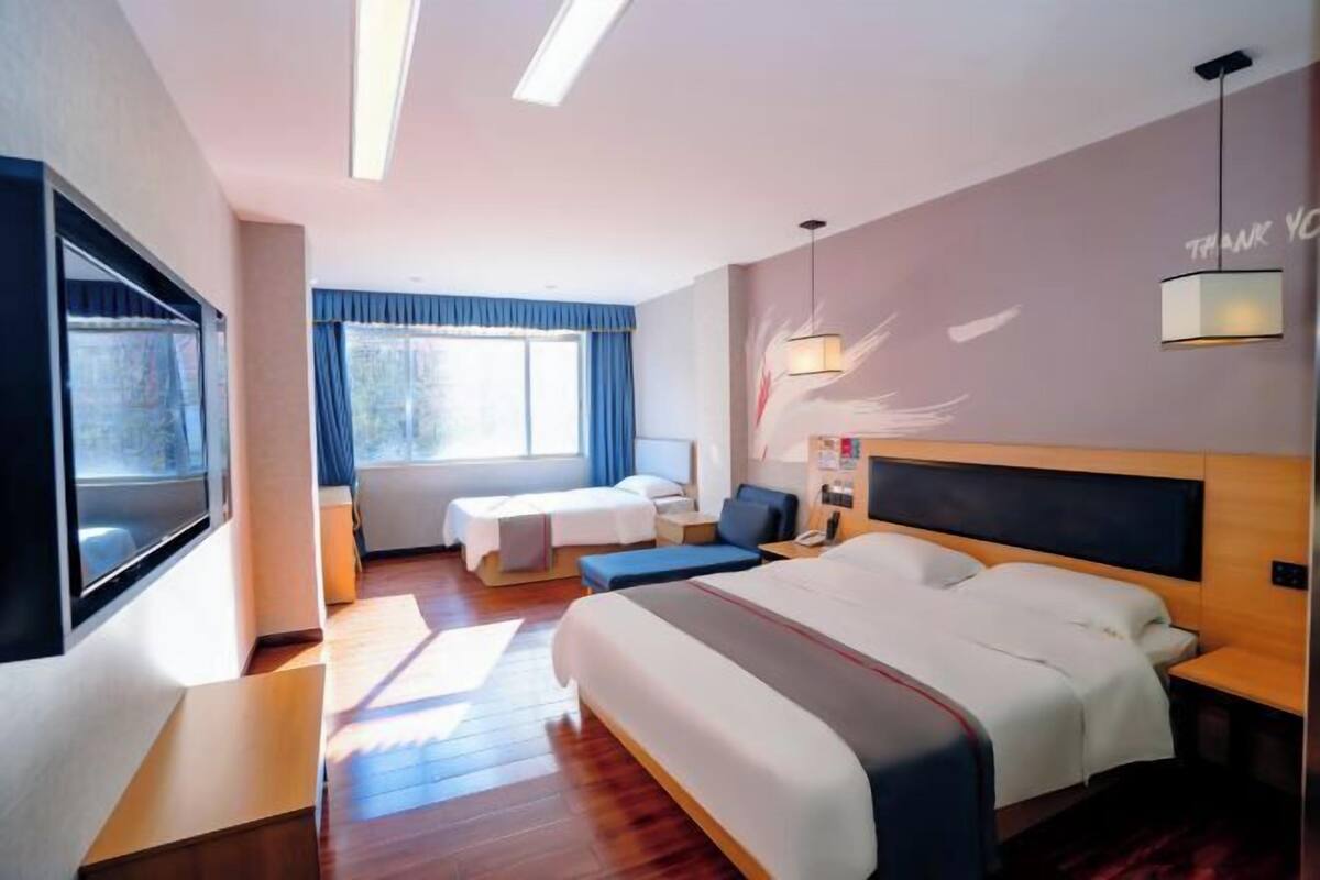 A modern hotel room with a large bed, a desk, a chair, a TV, and a window with curtains.
