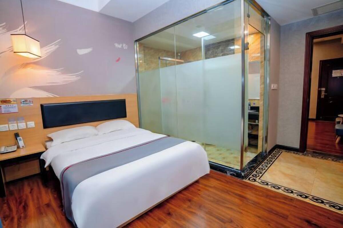 A hotel room with a bed, bedside table, and a glass partition wall.