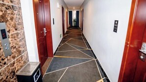 A hotel hallway with a geometric patterned carpet, wooden doors, and a trash bin. - Shankee Chain Hotel (Xinyi Zhongxing Avenue) (Xinyi)