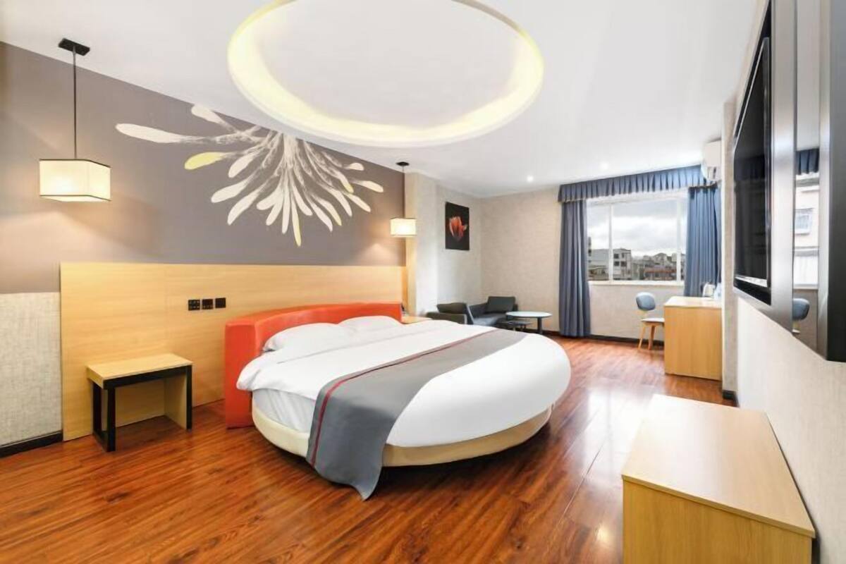 A modern hotel room with a large bed, a desk, and a view of the city.