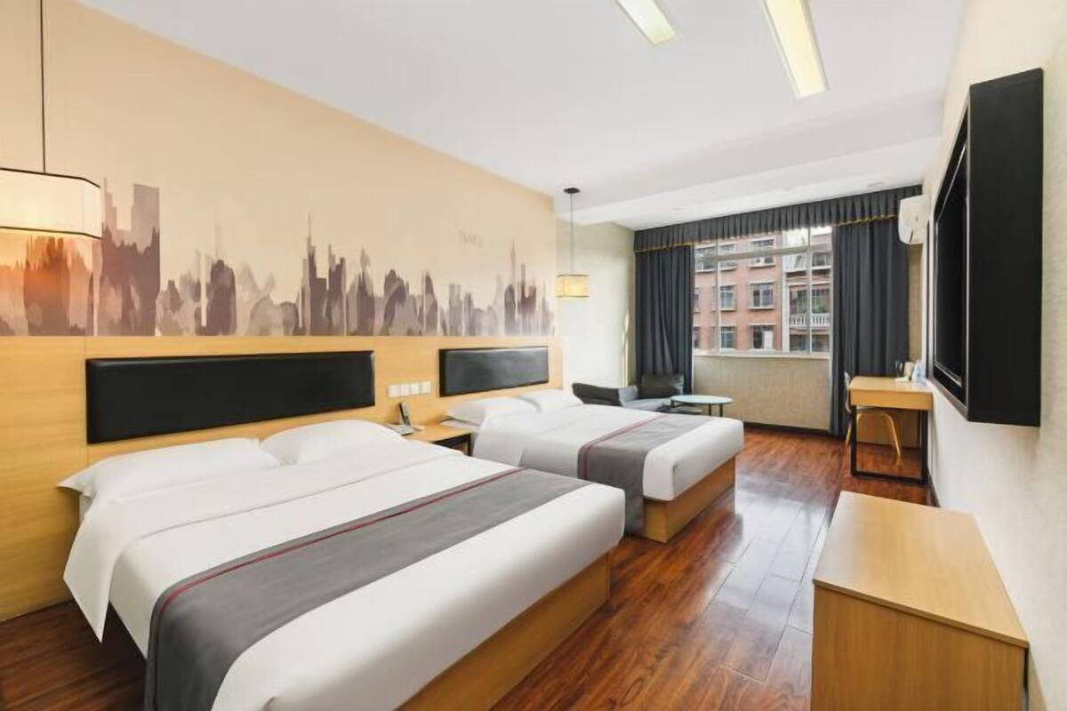 A hotel room with two beds, a desk, a chair, and a cityscape mural on the wall.