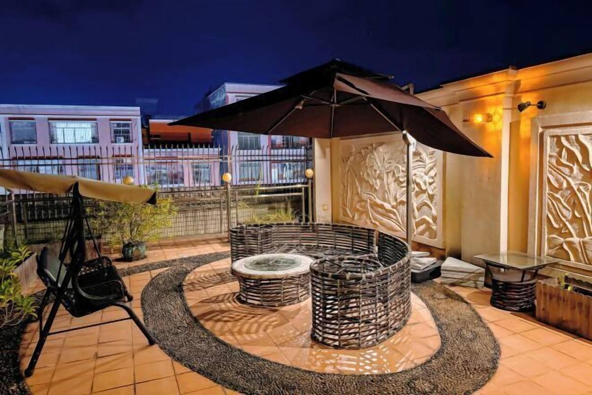 An outdoor seating area with wicker furniture, a central fire pit, and a large umbrella.