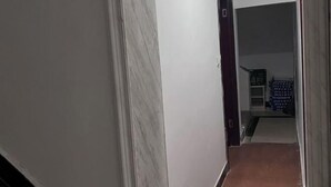 Un couloir étroit, avec un mur de marbre sur la gauche et un mur uni sur la droite. On aperçoit une porte au loin, qui donne sur une autre pièce.