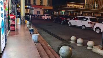 A street view at night with a sidewalk, parked cars, and buildings with illuminated signs.