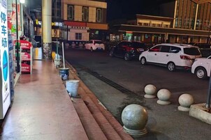 Une vue de rue de nuit, avec un trottoir, des voitures garées et des bâtiments dont les enseignes sont illuminées.