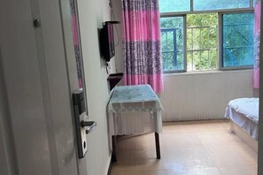 Una habitación con cama, mesa, televisor y ventana con cortinas.
