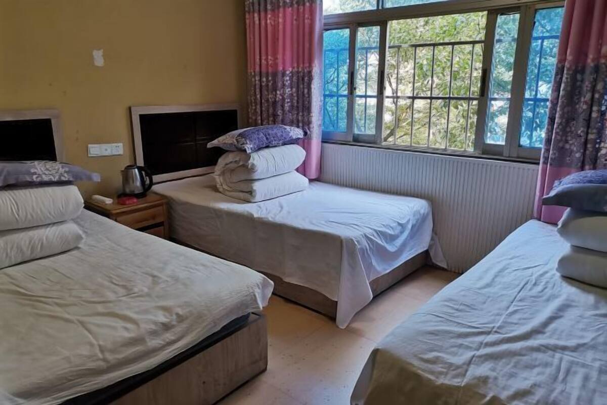 Ein Zimmer mit zwei Betten, einem Nachttisch mit Wasserkocher und einem Fenster mit Blick auf Grünflächen.
