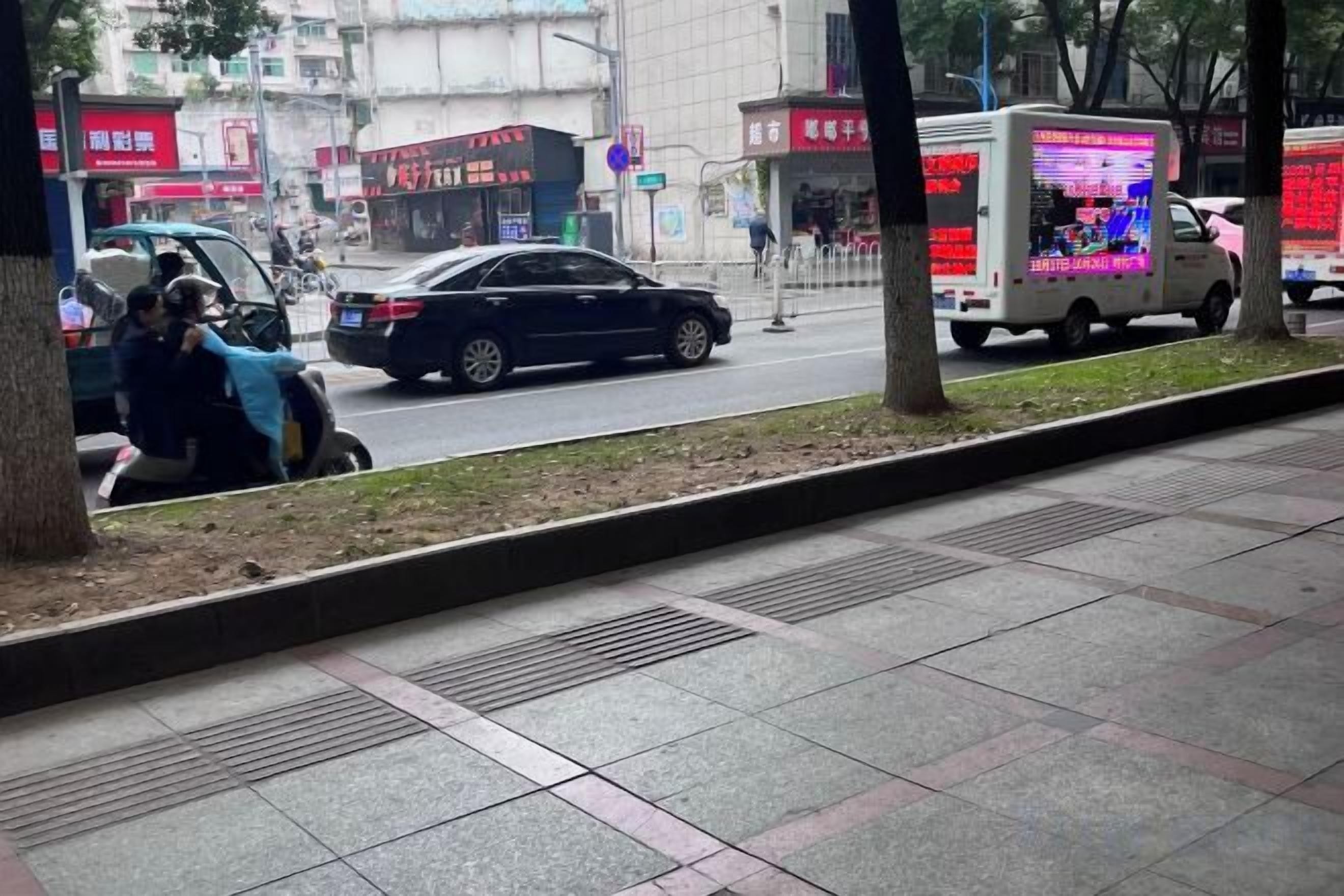 A street view with a sidewalk, trees, and a parked car.