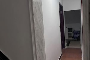 A narrow hallway with a door at the end leading to a room with a bed and a window.