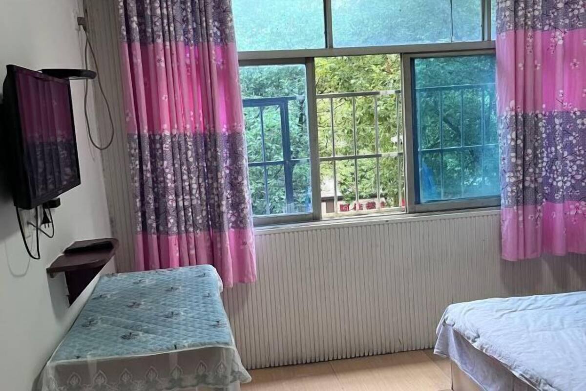 Ein Schlafzimmer mit Fenster, Heizkörper, Bett und Fernseher.