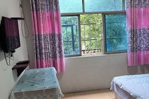 A bedroom with a window, a radiator, a bed, and a television.