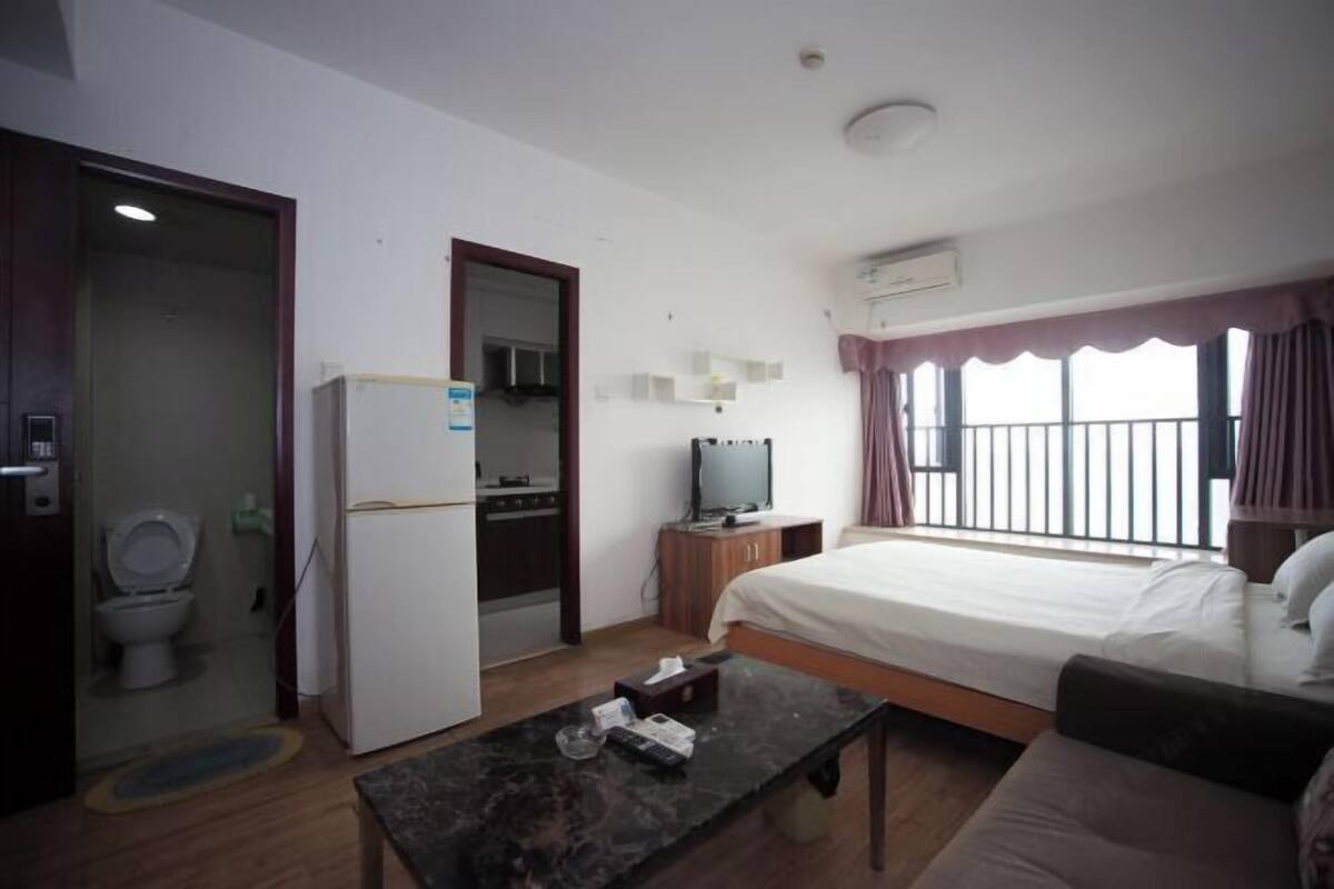 Habitación de hotel con cama, escritorio, televisor, refrigerador, baño y balcón.
