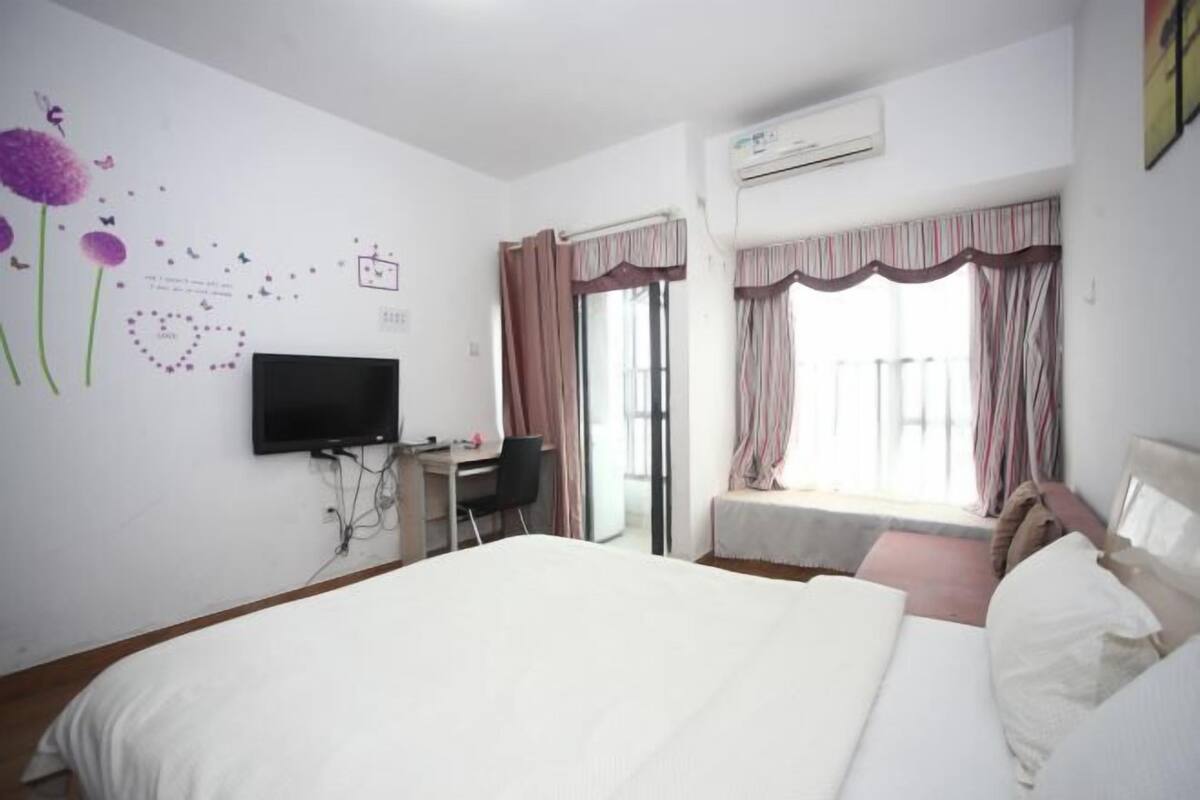 Habitación de hotel con cama, escritorio, televisor y ventana con cortinas.