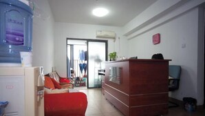 A room with a red sofa, a wooden cabinet, a water dispenser, and a view of a hallway with a sliding door. - YouJia Apartment (Foshan)