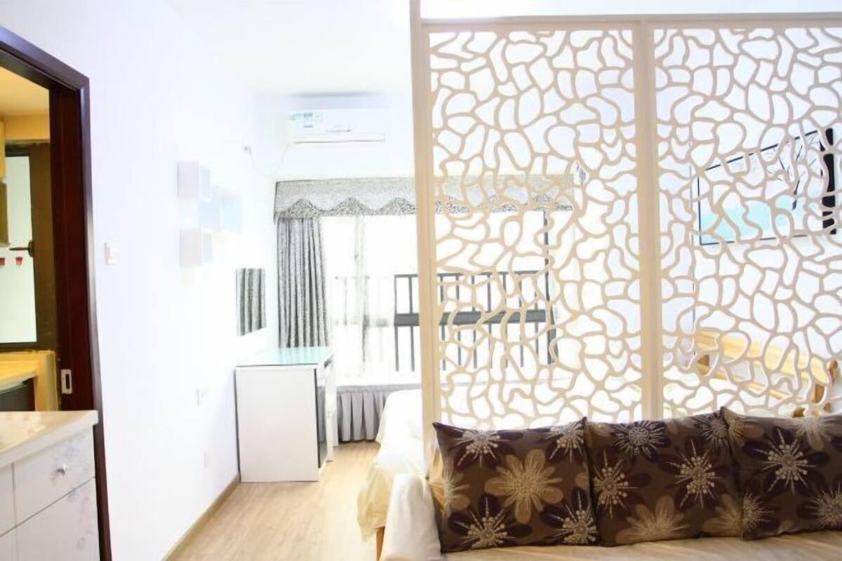 Una habitación con una cama, un armario blanco, una mesita pequeña y un biombo decorativo.